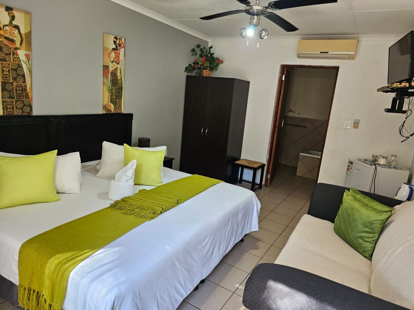 Bright double room with lime green throw, wardrobe, couch, air conditioner and en-suite bathroom