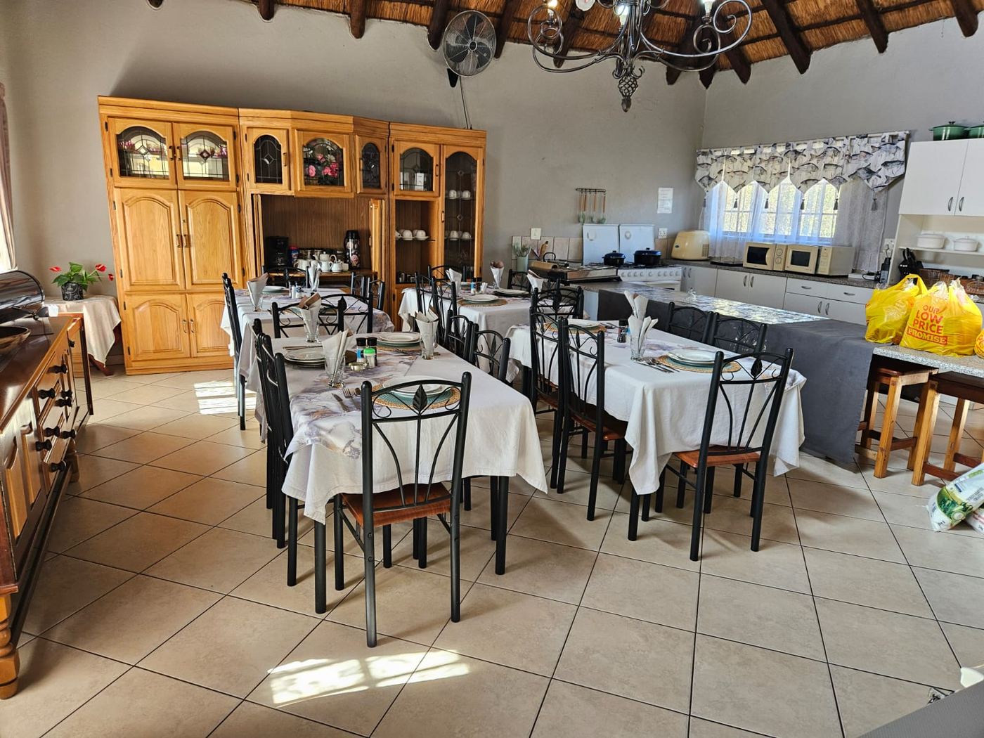 Thatched dining room with set tables, wooden display cabinets and an open kitchen